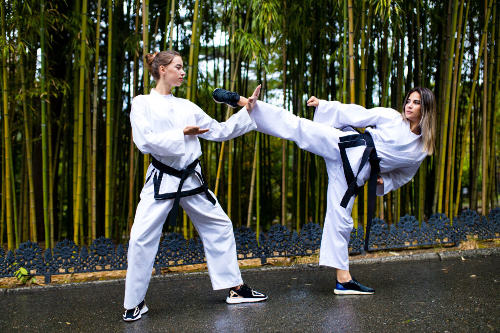 Two young women practicing martial arts at a summer camp, surrounded by bamboo trees.