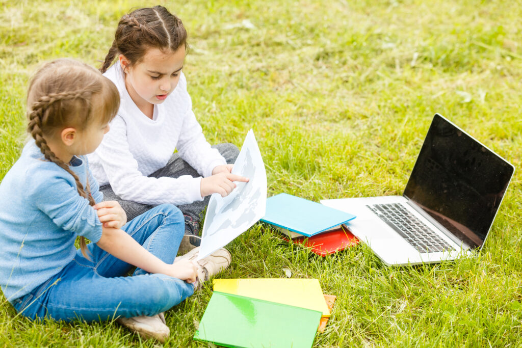 Children enjoying outdoor learning at summer camp with books and laptop.
