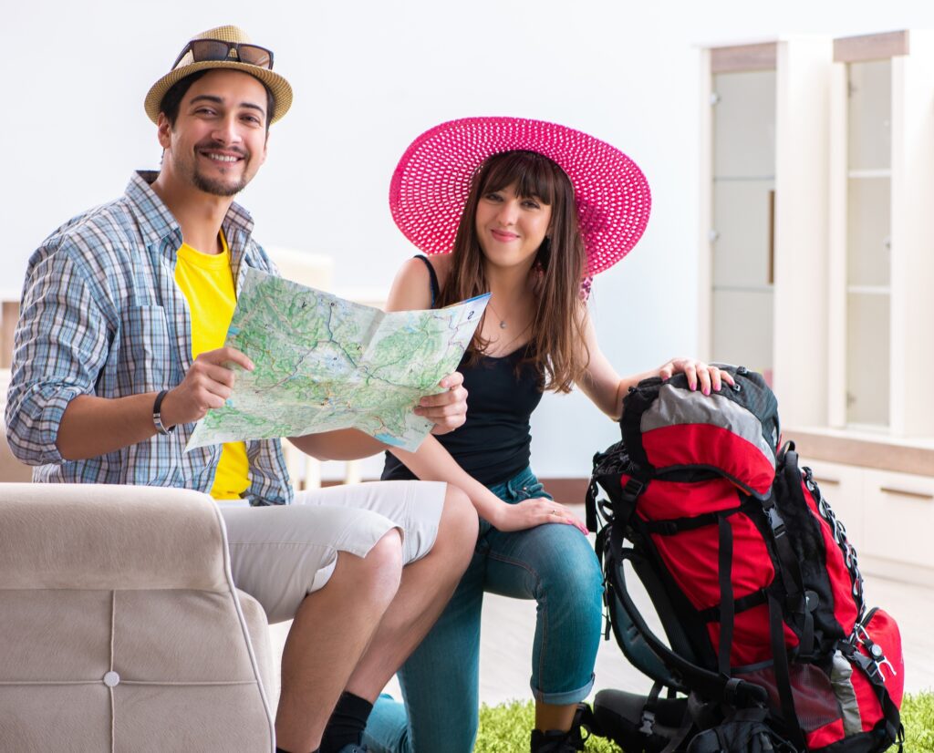 Two smiling campers planning a summer adventure with a map and backpack in a cozy room.