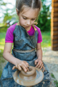 Young girl crafting pottery outdoors at summer camp, focusing on art and creativity.