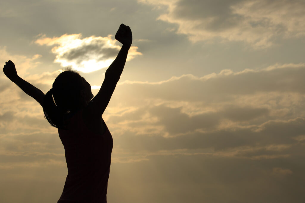 Camper enjoying a summer sunrise with arms raised, symbolizing freedom and happiness at camp.