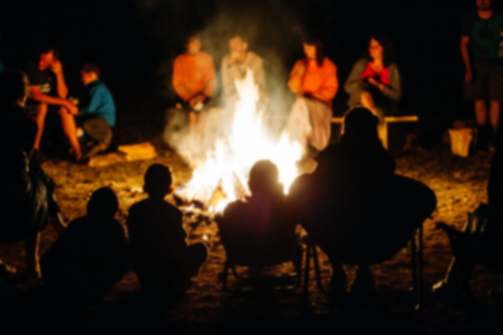 Campers gathered around a campfire at night, sharing stories, in a fun summer camp experience.