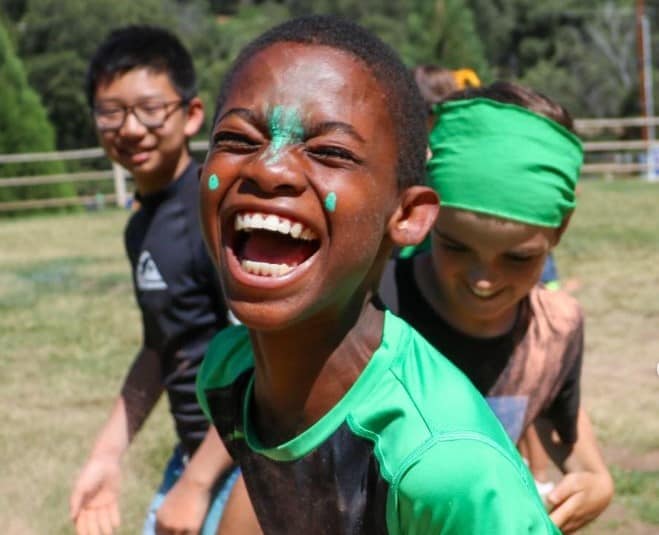 Kids laughing and playing outdoors at summer camp, enjoying fun activities and making friends.