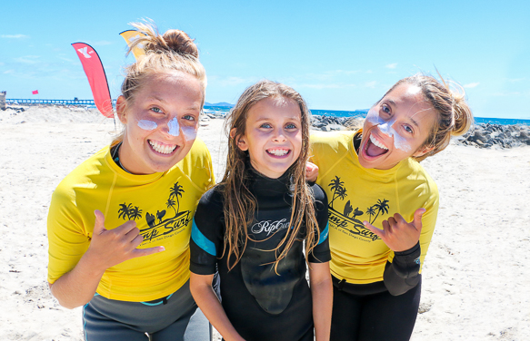 Young girl enjoying a fun beach day at a surf summer camp with two smiling instructors in yellow shirts.