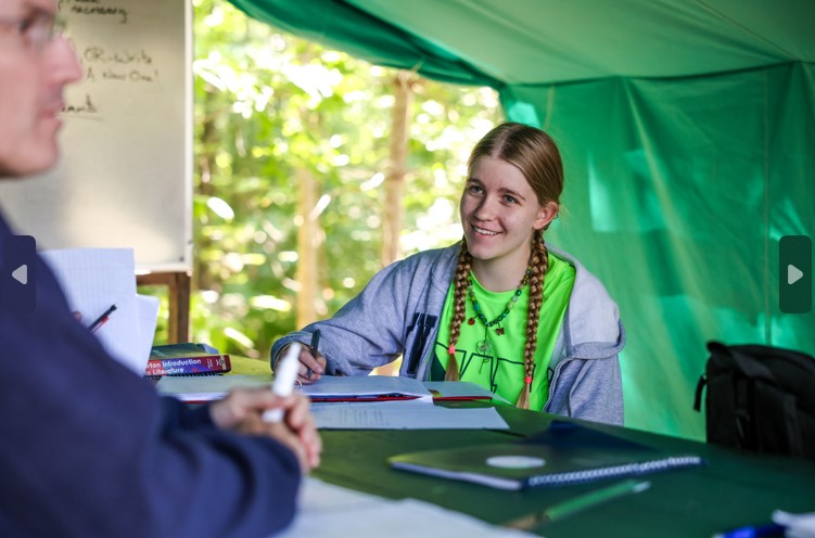 Smiling camper engaging in a summer camp workshop outdoors, surrounded by nature and learning materials. Smiling camper engaging in a summer camp workshop outdoors, surrounded by nature and learning materials.