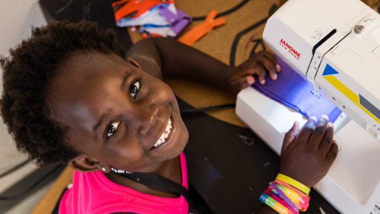 Child smiling while sewing at summer camp craft activity. Explore various engaging summer camp options for kids.