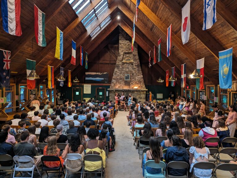 Campers gather in a flag-decorated hall for a summer camp activity, fostering community and cultural exchange. Campers gather in a flag-decorated hall for a summer camp activity, fostering community and cultural exchange.