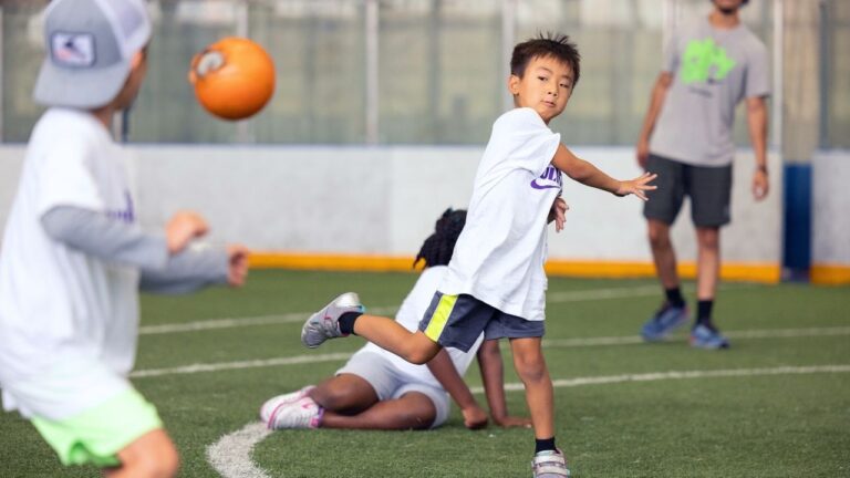 Children playing dodgeball at summer camp, having fun indoors on a field.