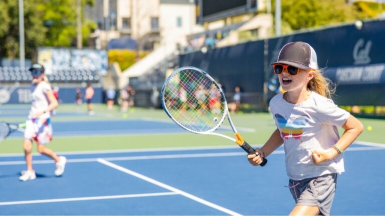 Child enjoying tennis at a summer camp tennis court, smiling and holding a racket. Perfect summer camp activity!