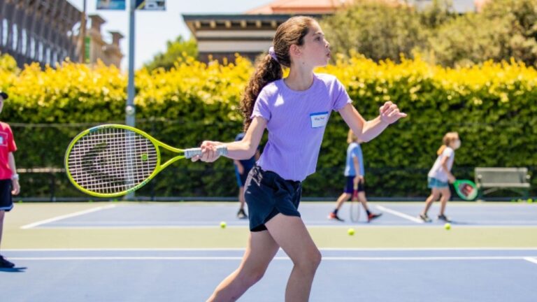 Girl playing tennis at summer camp, learning skills on a sunny outdoor court.