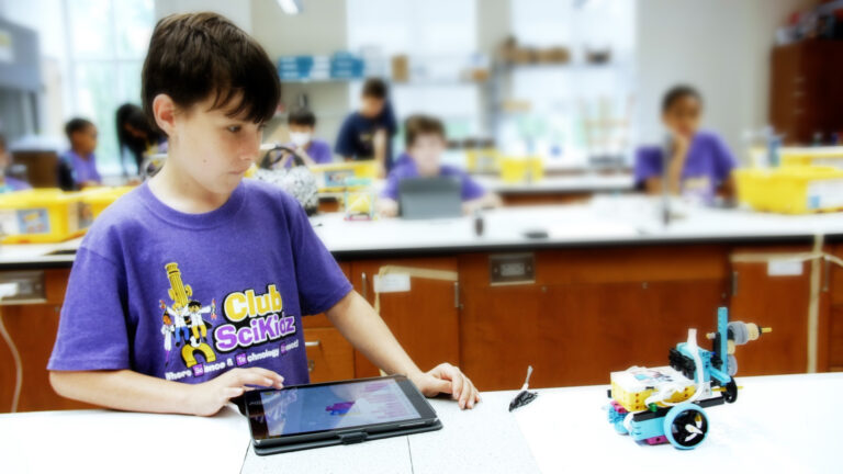 Child at summer camp learning robotics with tablet in classroom setting; hands-on STEM education experience. Child at summer camp learning robotics with tablet in classroom setting; hands-on STEM education experience.