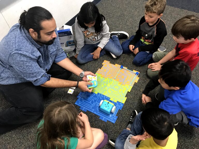 Children engaged in a summer camp STEM activity learning robotics, guided by an instructor. Children engaged in a summer camp STEM activity learning robotics, guided by an instructor.