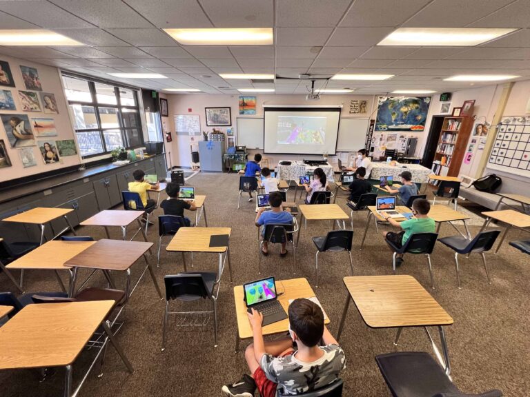 Children engaged in a tech class at summer camp, learning with laptops in a lively classroom setting.