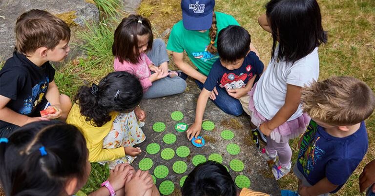 Children playing a board game outdoors at summer camp, fostering teamwork and friendship.