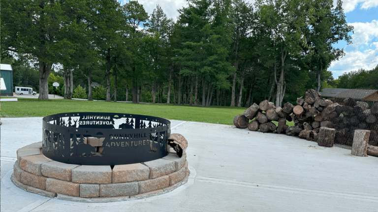 Fire pit at Sunnyhill Adventures summer camp with chopped wood and trees, perfect for outdoor activities. Fire pit at Sunnyhill Adventures summer camp with chopped wood and trees, perfect for outdoor activities.