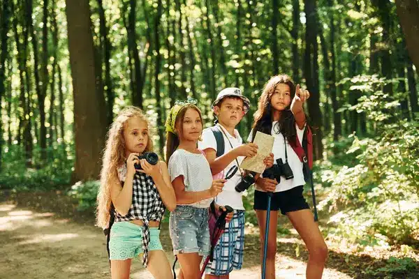 Children exploring nature with maps and cameras at summer camp in the forest.