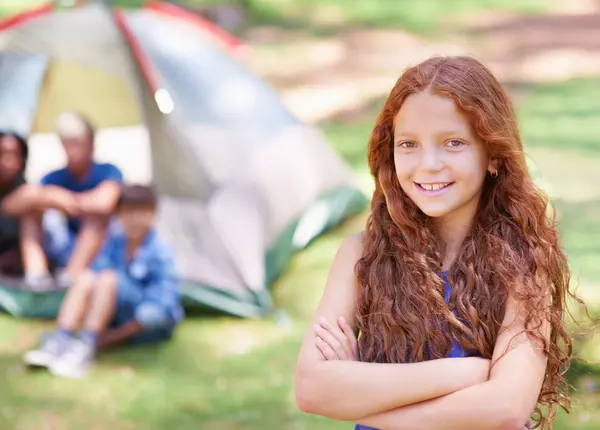 Smiling girl at summer camp with friends by tent in background, enjoying outdoor activities and friendship.