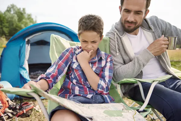 Boy and man studying map at camp with blue tent. Explore top summer camps for outdoor adventures.