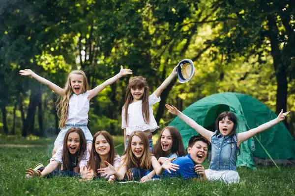 Group of happy kids enjoying summer camp activities near a tent in a forest setting.