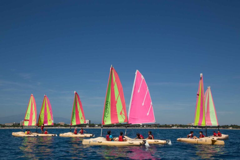 Kids sailing colorful boats at summer camp under clear blue sky.