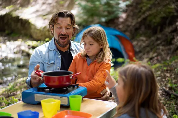 Kids cooking with an instructor at summer camp, enjoying outdoor activities by a tent in the woods.