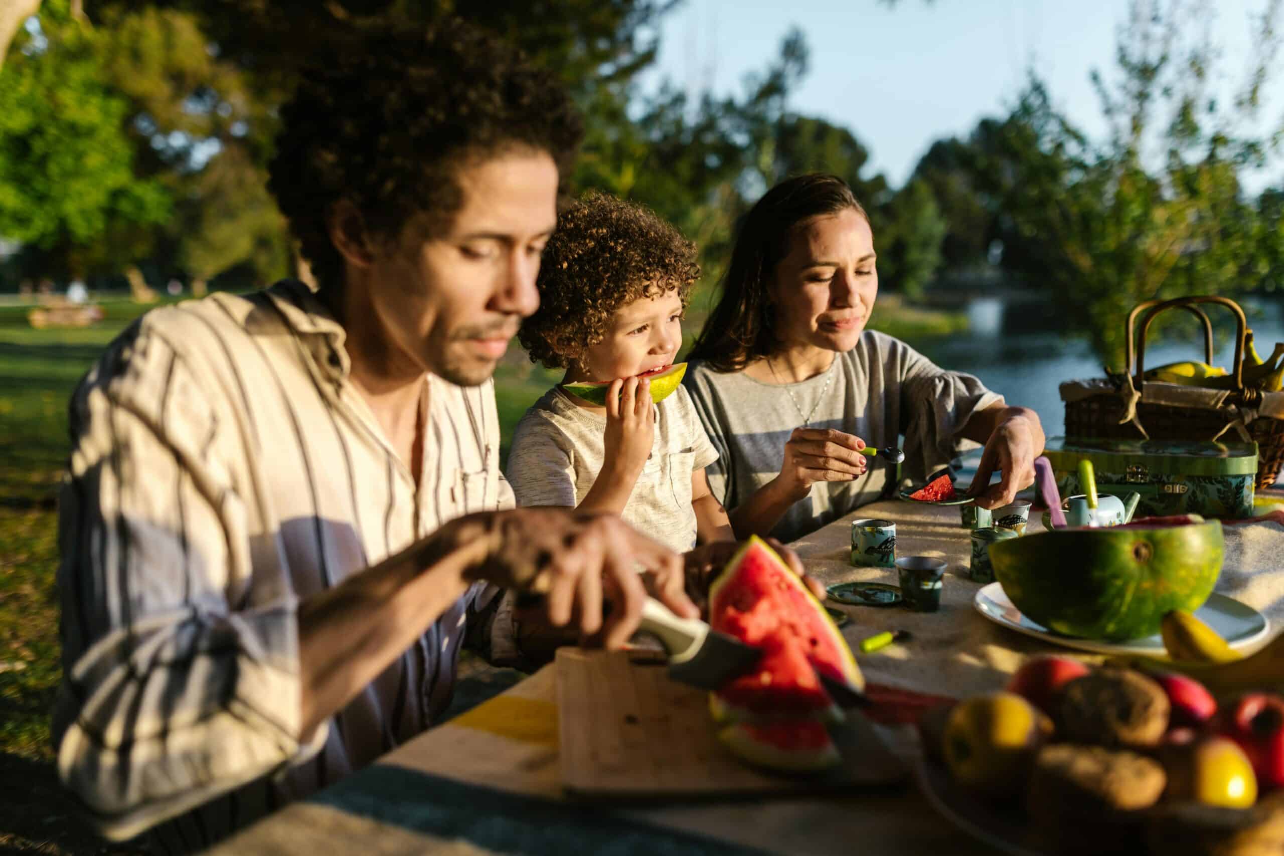Family enjoying a picnic with watermelon at summer camp by a lake. Perfect outdoor fun for kids and parents.