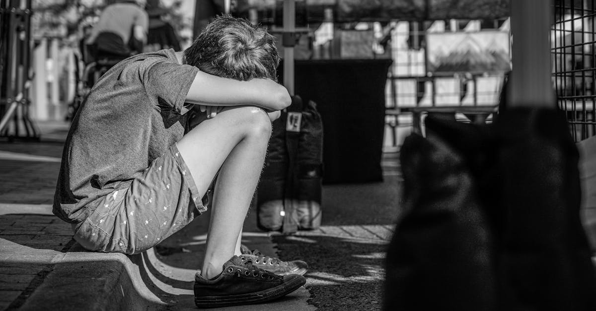 Child sitting alone, head on knees, at summer camp street event. Explore engaging summer camps for kids.