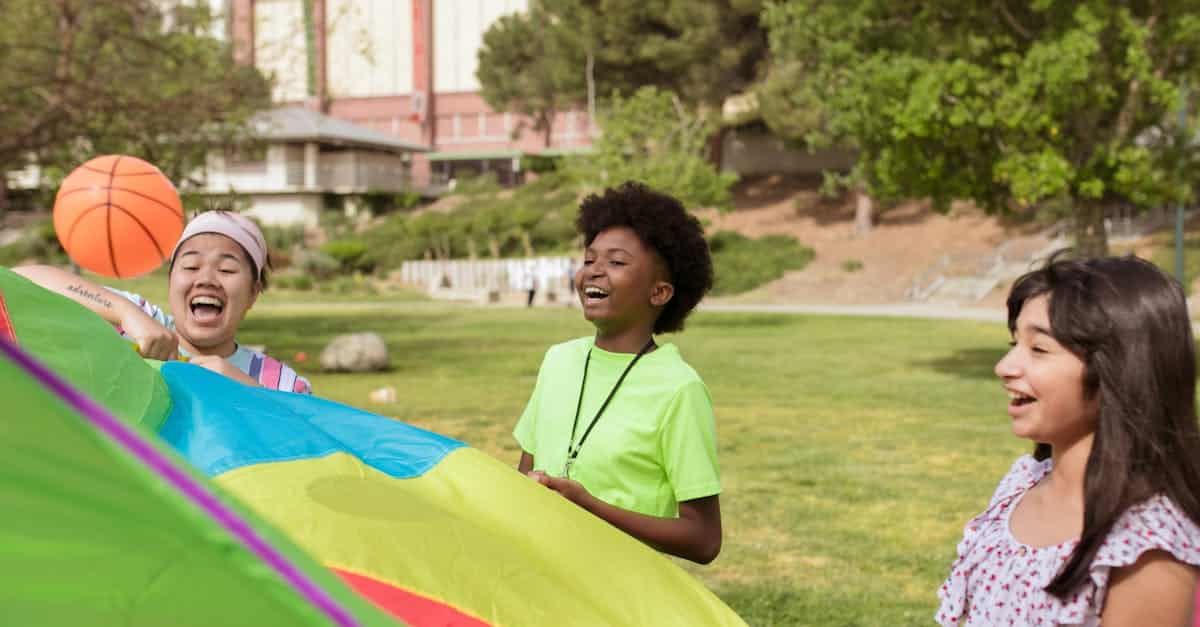 Kids enjoying outdoor activities with a colorful parachute at summer camp.