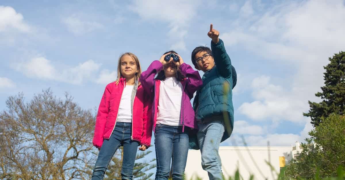Three kids exploring nature at a summer camp, one looking through binoculars, another pointing at the sky.