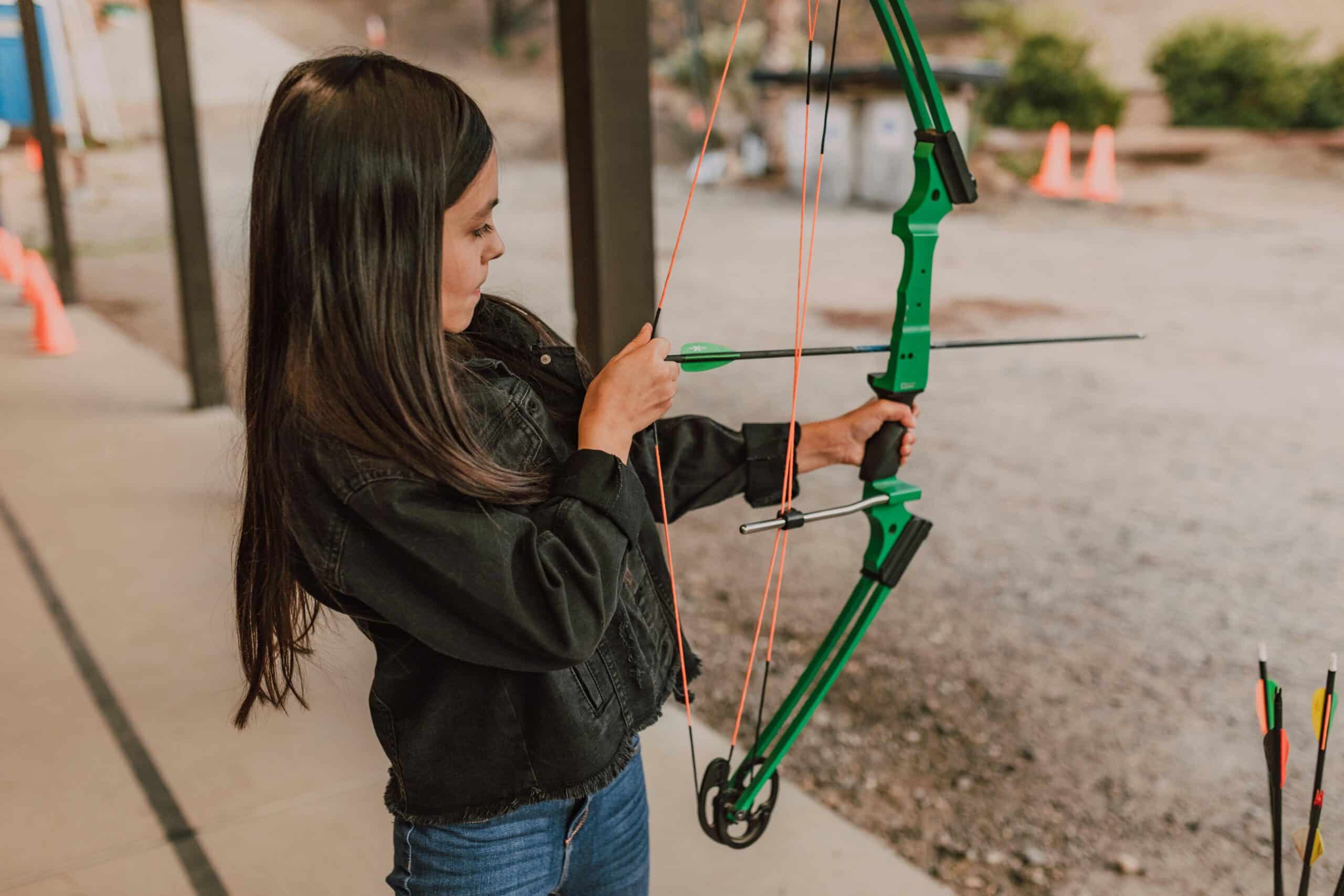 Child practicing archery at summer camp, focusing intently on drawing the bowstring.