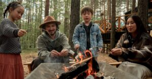 Family enjoying roasting marshmallows over campfire at summer camp in the woods.