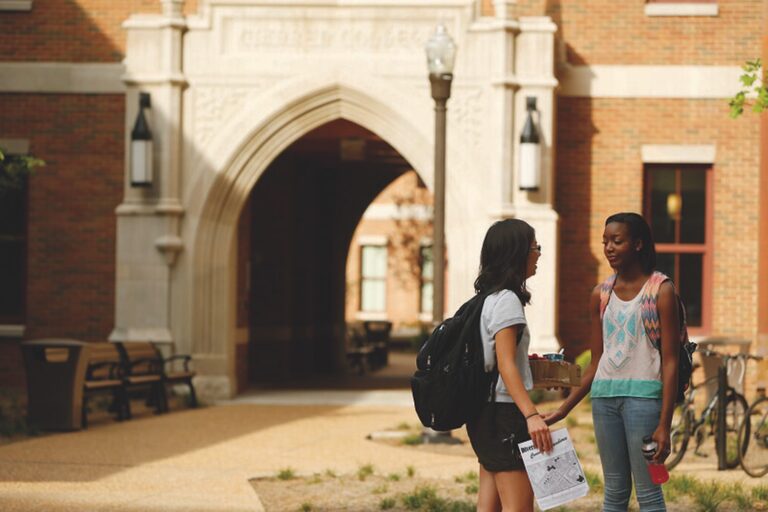 Two teen campers with backpacks chatting at summer camp campus entrance, holding map and snacks Two teen campers with backpacks chatting at summer camp campus entrance, holding map and snacks