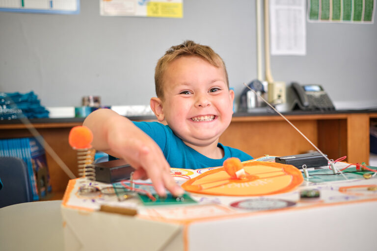 Smiling child engaging in hands-on STEM activity at summer camp, showcasing creativity and enthusiasm for learning. Smiling child engaging in hands-on STEM activity at summer camp, showcasing creativity and enthusiasm for learning.