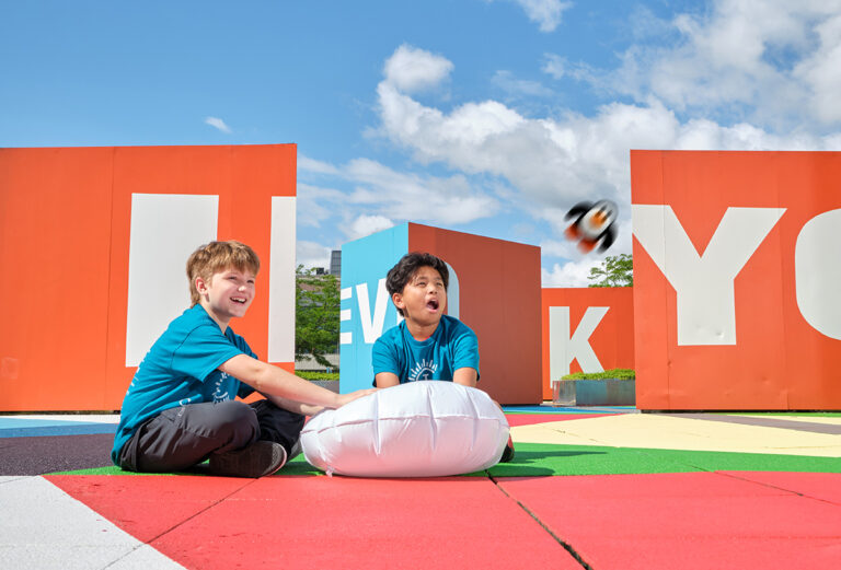 Two boys in colorful shirts play with a pillow in a vibrant outdoor setting at a summer camp. Fun and joy abound! Two boys in colorful shirts play with a pillow in a vibrant outdoor setting at a summer camp. Fun and joy abound!