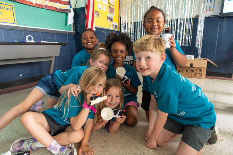 A group of happy children in matching camp shirts, smiling and holding crafts at a summer camp activity. A group of happy children in matching camp shirts, smiling and holding crafts at a summer camp activity.
