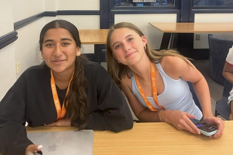 Two smiling teen campers wearing orange summer camp lanyards at a table with a laptop and smartphone Two smiling teen campers wearing orange summer camp lanyards at a table with a laptop and smartphone