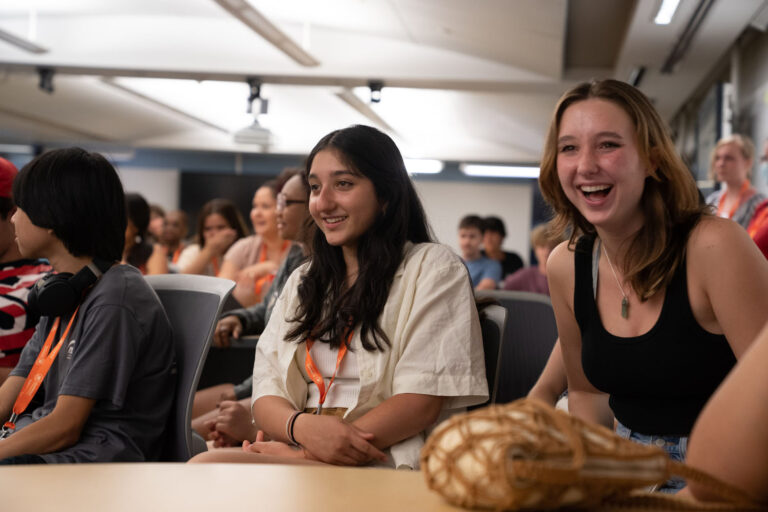 Teen campers wearing orange lanyards smiling and listening during an indoor summer camp workshop. Teen campers wearing orange lanyards smiling and listening during an indoor summer camp workshop.