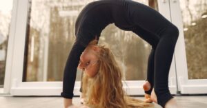 Young girl performing a flexible gymnastic pose at summer camp, showcasing strength and balance indoors.