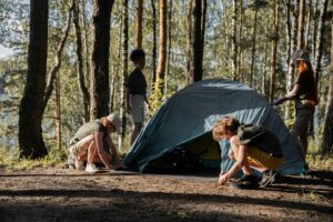 Campers setting up a tent at summer camp in a shaded forest campsite by a lake